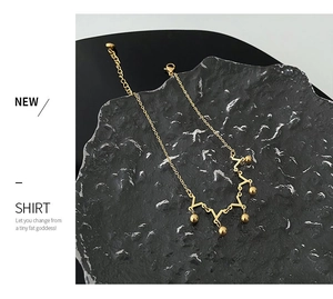 Detail view of gold titanium crown anklet with V-shape design and round sphere pendants