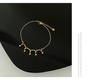 Detail of gold crown-style anklet featuring V-shaped links and polished metal beads