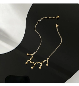 Detailed view of a gold titanium crown anklet with five hanging beads on black background
