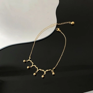 Golden crown-style anklet with V-shaped links and hanging beads on a modern tray