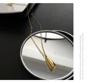 Gros plan d'un collier pendentif goutte d'or poli avec une finition miroir réfléchissante