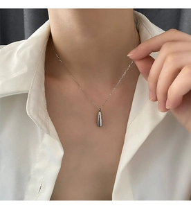 Pendentif en forme de goutte d'argent poli porté par un mannequin en chemise blanche