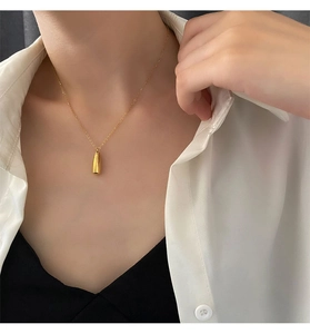 Détail d'un pendentif flacon de parfum doré sur une chaîne délicate porté par un mannequin