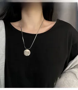 Chaîne serpent argentée avec pendentif rond gravé D et Dreaming sur un t-shirt noir