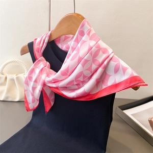 Close-up of pink floral silk scarf tied to a navy top on a wooden hanger with pearls