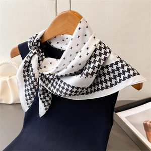 Détail d'un foulard en soie à motif pied-de-poule noué sur un débardeur en tricot sombre