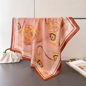 Detail of pink silk scarf with gold chain print and baroque pattern draped on a rack
