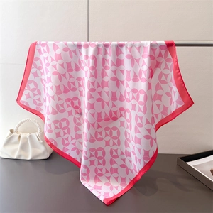 Pink and white geometric silk scarf displayed hanging next to a white pearl handbag
