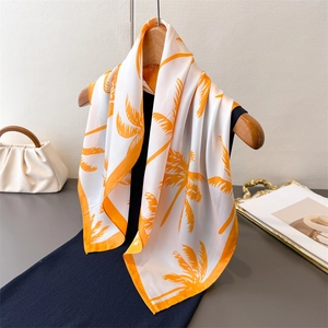 Elegant silk scarf with orange palm print hanging on hanger with a stylish handbag