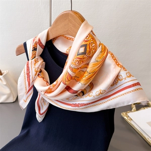 Close-up of silk scarf with orange chain prints styled on a navy knit vest neckline