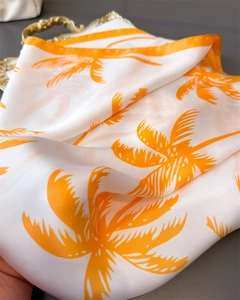 Detailed macro of floral silk scarf featuring orange palm tree prints on white satin