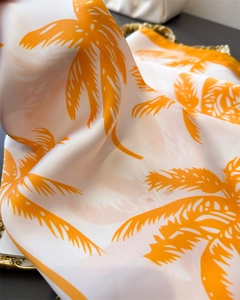 Detail of silk-like scarf featuring orange palm leaf prints on a cream background