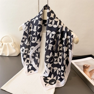 Elegant black and white geometric print silk scarf displayed on a white knit vest