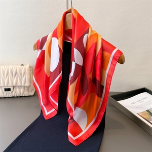 Carré en soie aux motifs géométriques rouge et orange drapé sur un cintre en bois chic