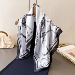 Elegant silk scarf with black and white chain pattern hanging on a wooden hanger