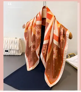 Detail of silk-like scarf with orange and brown geometric star print hanging on a hanger