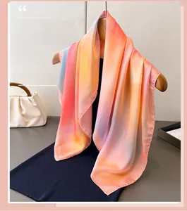 Detail of gradient satin silk scarf with orange and blue tones hanging on a wooden hanger