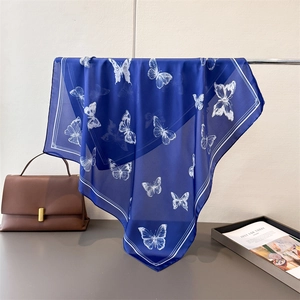 Close-up of royal blue silk scarf with white butterfly print draped over a bag