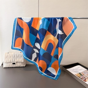 Détail d'un foulard carré en soie avec imprimé géométrique drapé sur un support en métal