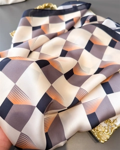 Détail d'un foulard en soie à carreaux géométriques posé sur un plateau doré vintage