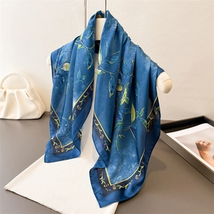 Elegant blue silk scarf with botanical leaf prints hanging on a white hanger