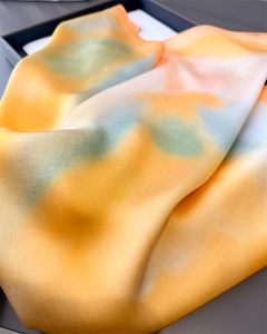 Detailed close-up of gradient silk scarf with orange and teal satin fabric texture