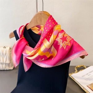 Silk scarf with pink geometric prints and star patterns styled on a wooden hanger