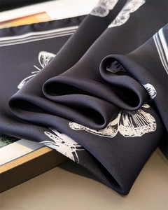 Detail of premium black silk-like scarf with white butterfly prints and soft fabric folds