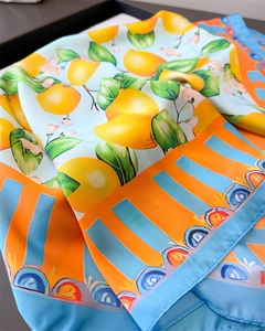 Detailed view of silk-like scarf featuring lemon prints and orange decorative borders