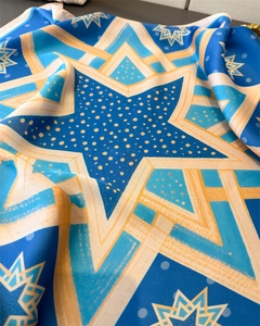 Close-up of geometric silk scarf with navy blue and yellow star patterns and silky texture