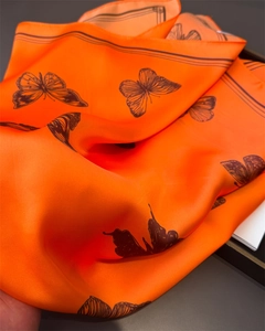 Macro detail of silk-like orange scarf showing satin texture and butterfly print