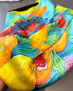Close-up of silk scarf with lemon cherry print and fine stitching on blue fabric