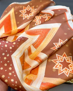 Macro detail of silk-like satin fabric with orange and brown geometric star patterns