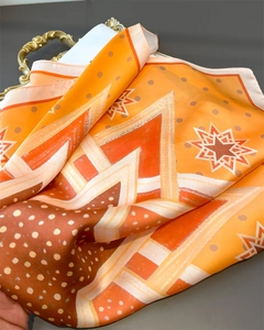 Close-up of geometric silk-like scarf with orange and brown star patterns on a gold tray
