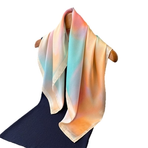 Elegant gradient silk-like scarf in sunset hues of orange and pink hanging on a wooden hanger