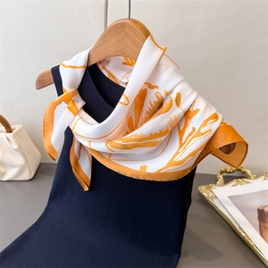 Detail showing an elegant white and orange floral faux silk scarf tied on a blue knit top