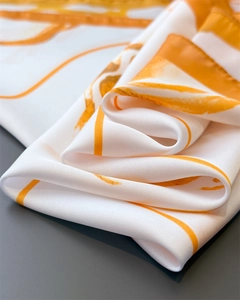 Detailed view of folded silk-texture scarf featuring orange and gold abstract stripe patterns