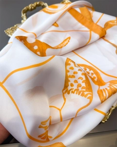 Detail of silk scarf with orange patterns on ivory base in a golden tray