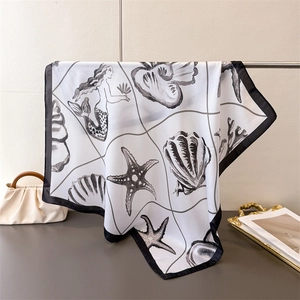 Detail of silk square scarf featuring black mermaid and seashell patterns on white silk