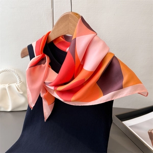 Elegant geometric silk scarf in orange and pink tied on a black tank top with pearl handbag