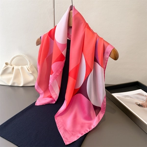 Elegant geometric silk-like scarf with pink and red patterns on a wooden hanger