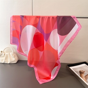 Close-up of geometric silk-like square scarf in pink and red tones on a metal hanger