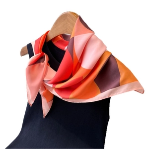 Elegant geometric print silk scarf in orange and red tones on a wooden hanger
