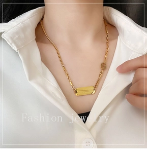 Detailed view of a gold titanium steel necklace with a rectangular engraved pendant on a shirt