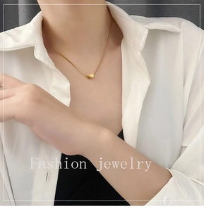 Detail of a minimalist gold snake chain necklace with an oval bead pendant on a model