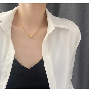 Close-up of a minimalist gold geometric pendant necklace worn on a white shirt