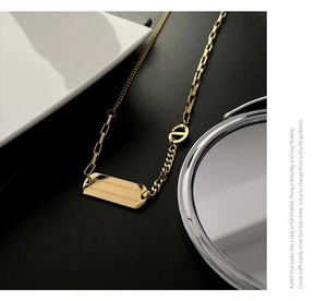 Detail of gold titanium steel necklace with rectangular pendant and engraved text