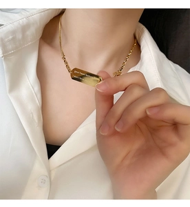 Detailed close-up of gold titanium steel necklace featuring an engraved rectangular pendant
