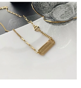 Close-up of gold titanium steel pendant necklace with engraved tag on ceramic plate