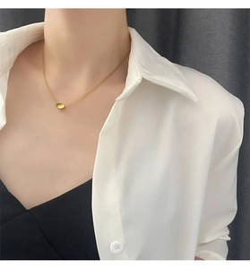 Close-up of minimalist gold bean pendant on a fine box chain necklace worn by a model